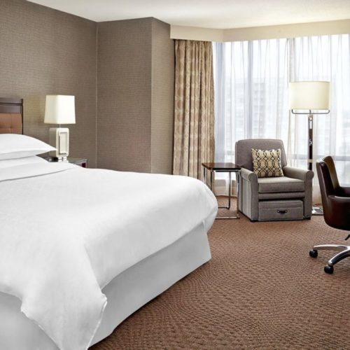 Elegant hotel room with a king-size bed, armchair, and modern amenities.