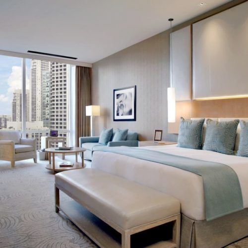 Elegant modern hotel room with city view, plush bedding, and sitting area.